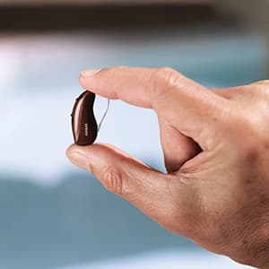 Mão segurando aparelho auditivo em close.